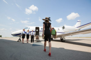 Rear view of woman walking towards private jet while pilot and stewardesses standing at airport terminal